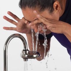 a woman drinking water from a faucet in front of her face and hands