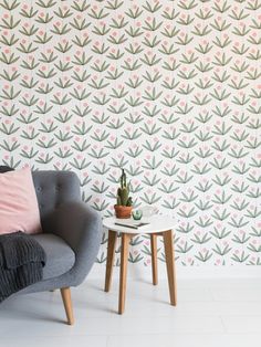 a grey chair sitting next to a table with a plant on it and a wall paper behind it