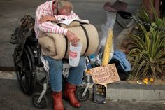 a man sitting in a wheel chair next to a pile of garbage and a sign that says we don't have a poverty problem