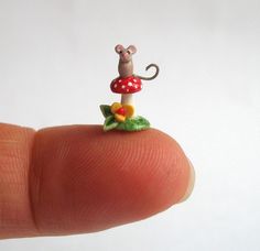 a tiny mouse figurine sitting on top of a small mushroom with leaves and flowers