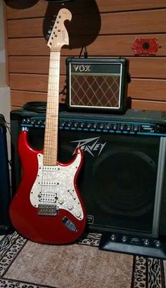 a red electric guitar sitting next to an amp