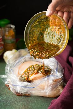 a person pouring sauce on some food in a glass bowl with another hand holding it