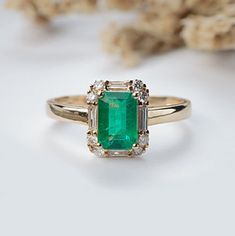 an emerald and diamond ring on a white surface