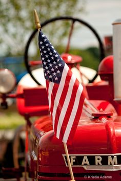 an american flag is placed on the hood of a red firetruck with farm equipment in the background