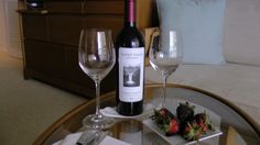 a glass table topped with two wine glasses next to a bottle of wine and strawberries