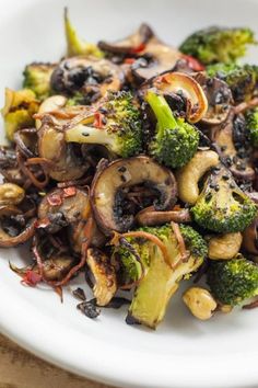 broccoli, mushrooms and other vegetables on a white plate sitting on a wooden table