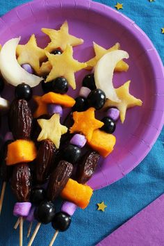 a purple plate topped with fruit and stars on skewers next to other food items