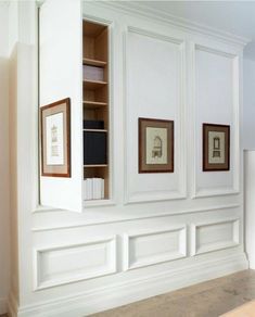 an empty room with white paneling and framed pictures on the wall, along with bookshelves