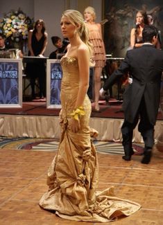 a woman in a gold dress standing on a wooden floor with other people around her