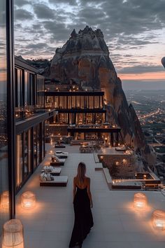 a woman standing on top of a tall building next to a mountain at night time