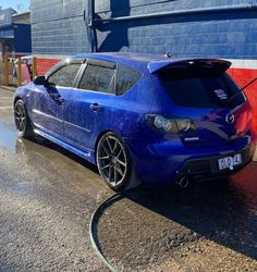 a blue car is parked in front of a red and white building with a hose attached to it