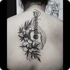 the back of a woman's neck with a guitar and flowers tattoo on it