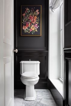 a white toilet sitting in a bathroom next to a black and white wall with flowers on it