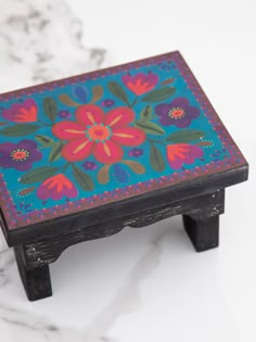 an artistically painted wooden stool with flowers on the top and bottom, sitting on a marble surface