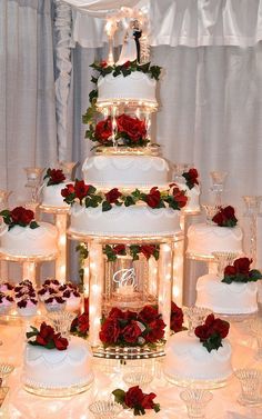 a wedding cake with red flowers and lights on the top is surrounded by other desserts