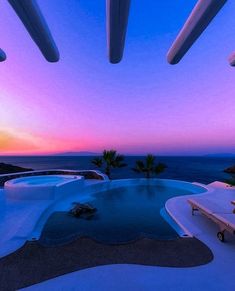 an outdoor swimming pool surrounded by lounge chairs and palm trees at sunset or dawn over the ocean