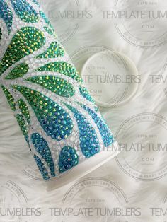 a coffee cup decorated with blue, green and white beaded decorations on a bed