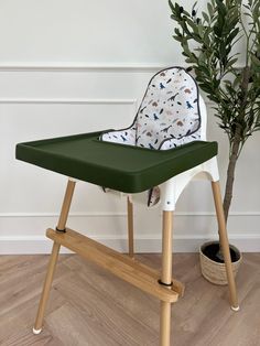 a green and white highchair next to a potted plant on the floor