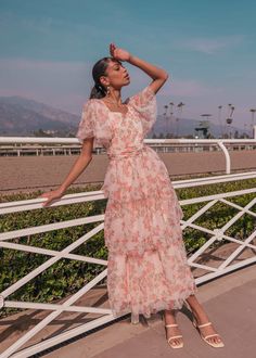 a woman in a pink dress leaning on a fence