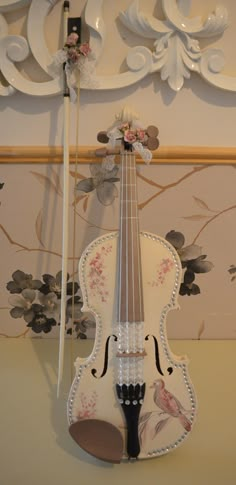 a white violin hanging from the side of a wall next to a flowered background