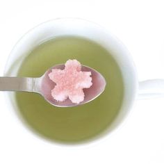 a spoon full of green tea with pink sugar in it and on top of the cup