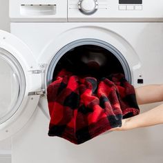 a person holding a red and black plaid cloth over a washing machine