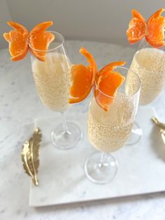 three glasses filled with orange slices on top of a white countertop next to gold utensils