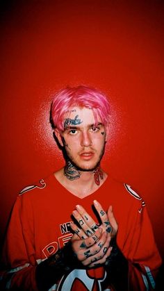 a man with pink hair and tattoos holding his hands up in front of the camera