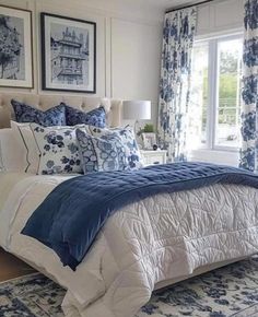 a bedroom with blue and white bedding, curtains and pictures on the wall above it