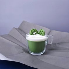 a cup filled with green liquid on top of a gray cloth covered table next to a napkin