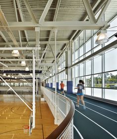 two people are walking in an indoor basketball court with wood floors and metal railings