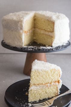 a white cake on a black plate with a slice taken out of it and the rest of the cake in the background