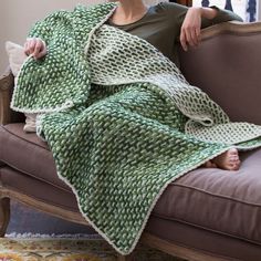 a woman is sitting on a couch wrapped in a green knitted blanket and looking out the window