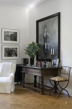 a white chair sitting next to a table with pictures on the wall and a vase filled with flowers