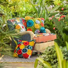 a chair with colorful pillows in the middle of some plants