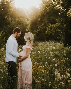 a pregnant woman standing next to a man in a field with wildflowers at sunset