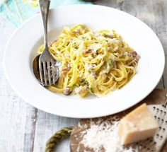 a white plate topped with pasta and cheese next to a fork on top of a wooden table