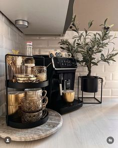 there is a coffee maker on the counter next to some cups and saucers in front of a potted plant