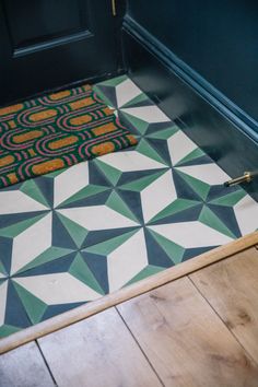 a door mat on the floor in front of a black door with a green and yellow design