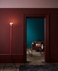 a red floor lamp sitting in the middle of a living room next to a blue wall