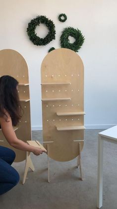 a woman kneeling down next to two wooden chairs with holes in the back and shelves on each side