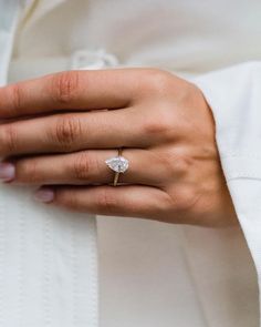 a woman's hand with a ring on her finger and a white shirt in the background