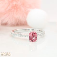 a pink diamond ring sitting on top of a white table next to a stuffed animal