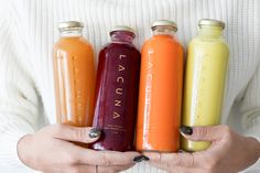 a woman holding four bottles of juice in her hands