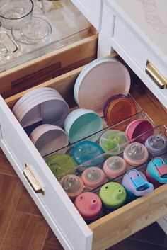 an open drawer filled with lots of different colored cups and saucer's in it