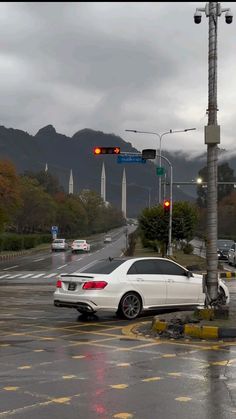 a white car is stopped at an intersection with traffic lights and mountains in the background