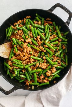 green beans and meat in a skillet with a wooden spatula on the side