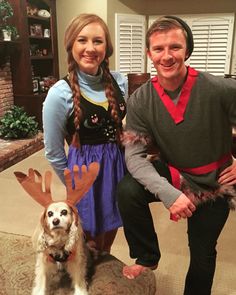 a man and woman standing next to a dog wearing reindeer antlers on their ears