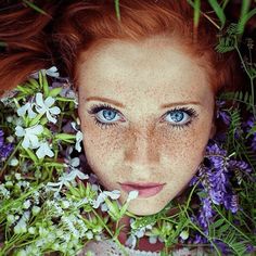 a woman with freckled hair and blue eyes surrounded by flowers