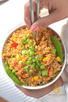 a person holding a bowl filled with rice and vegetables